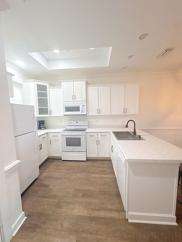 A modern kitchen with white cabinetry, a microwave, an oven, and a sink.