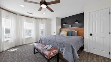 A bedroom with a bed, a bench, a ceiling fan, and a view of the outside.