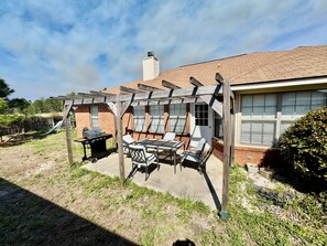 Un patio con una parrilla, mobiliario exterior y una estructura de pérgola.