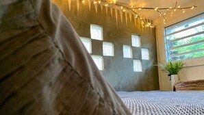 Ein Schlafzimmer mit gemustertem Bettzeug, einem Fenster mit vielen Glasscheiben und Lichterketten.