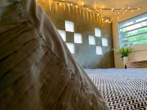 A bedroom with a patterned bedspread, a window with multiple panes, and string lights.