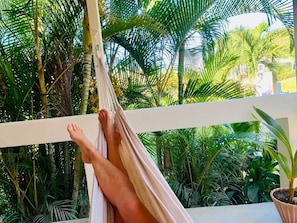A hammock on a balcony with lush greenery in the background.