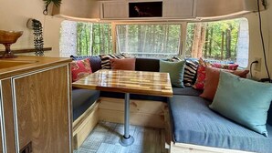 Ein gemütliches Blockhauss-Interieur mit einem Holztisch, einer eingebauten Bank mit Kissen und einem Fenster mit Blick auf einen Wald.