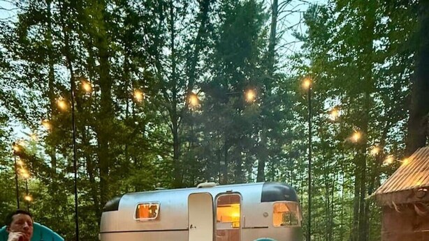 Ein Campingplatz mit Feuerstelle, einem Wohnwagen und einer kleinen Holzhütte.