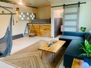 Ein gemütlicher Wohnbereich mit Sofa, Couchtisch, Hängematte, einer Holzbank und einer Küchenzeile.