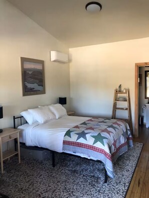Ein Schlafzimmer mit einem Bett, Nachttischen, einer Wand-Klimaanlage, einem Gemälde und einer Holzleiter.