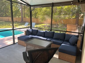Un espace extérieur aménagé, abrité et doté de sièges, avec vue sur la piscine, du mobilier en osier et une structure en verre.