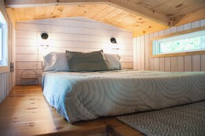Ein Schlafzimmer einer Holzhütte mit einem Bett, zwei Wandleuchten und einem Fenster.