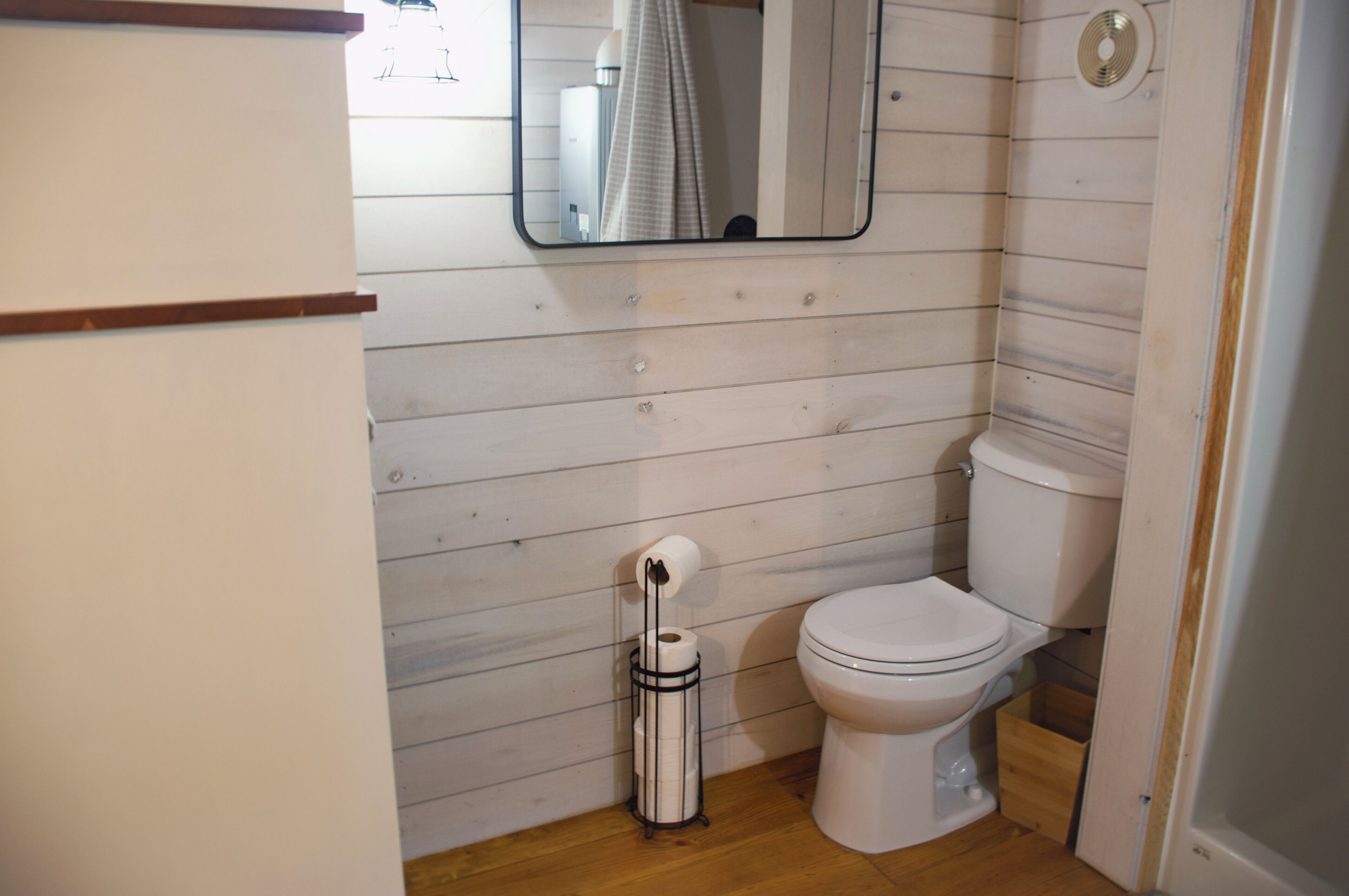 A bathroom with a toilet, a mirror, and a toilet paper holder.