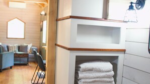A room with a wooden floor, a white built-in shelf with towels, a wicker basket, and a wooden ceiling. - Beautiful Secluded Tiny Home nestled in Huntingdon,Pa. Perfect couples getaway (Huntingdon)