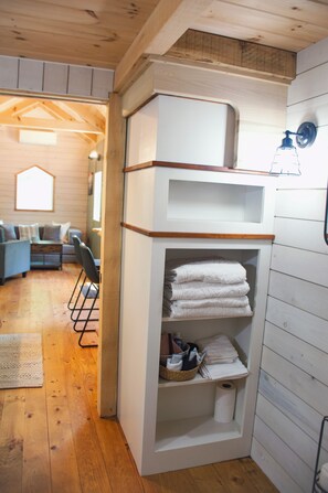 Ein Zimmer mit Holzboden, einer weißen, eingebauten Ablage mit Handtüchern, einem Korbwannen und einer Holzbalkendecke.