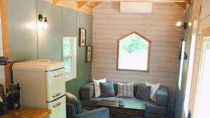 A compact kitchen with a refrigerator, a dining table set for two, and a sofa in the living area. - Beautiful Secluded Tiny Home nestled in Huntingdon,Pa. Perfect couples getaway (Huntingdon)