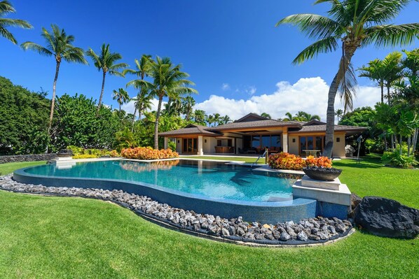 Ein Haus mit Swimmingpool, umgeben von Palmen und einem gepflegten Rasen.