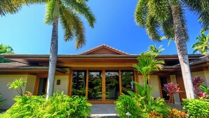 A house with a large glass door, surrounded by tropical plants and palm trees. - Spacious Ocean View Villa in Beautiful Mauna Lani Resort with AC (Mauna Lani Resort)