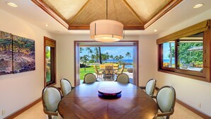A dining area with a round table, chairs, a hanging light fixture, and a view of a tropical landscape. - Spacious Ocean View Villa in Beautiful Mauna Lani Resort with AC (Mauna Lani Resort)