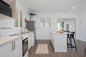 Eine moderne Küche mit weißen Schränken, einem Backofen, einer Spüle und einem Essbereich mit einem Barhocker.