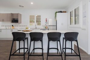 Eine moderne Küche mit weißen Schränken, einer zentralen Kochinsel mit Barhocker, einer Mikrowelle und einem Kühlschrank.