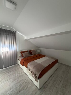 Een moderne slaapkamer met een schuine hemel, een groot bed met wit frame en een raam met verticale zonwering.