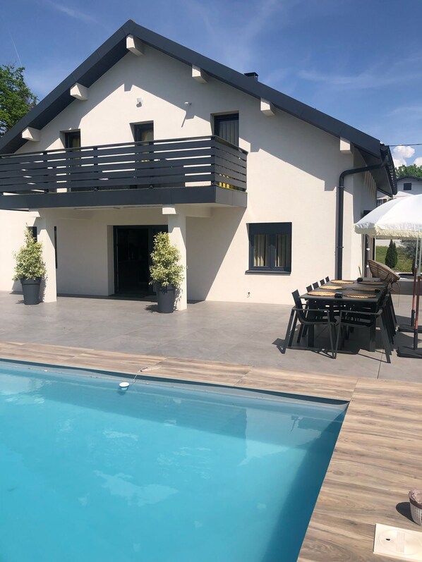 Una casa moderna de dos pisos con piscina, mobiliario exterior y plantas en macetas.