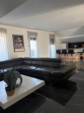 A modern living room with a sectional sofa, a white coffee table, and a dining area with a kitchen in the background. - Bao Lounge - Apartment T3 with Pool & Parking (Chavanod)