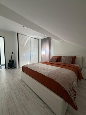 Un dormitorio moderno con una cama grande, una guitarra y un ventanal corredero que da a un balcón.
