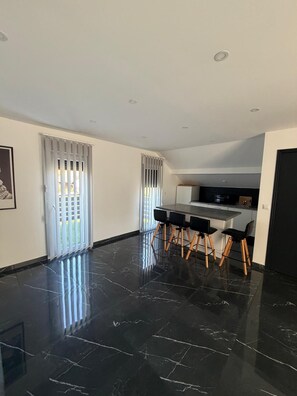Een moderne keuken met een donkere marmeren vloer, een eethoek met een tafel en stoelen, en een groot raam met jaloezieën.