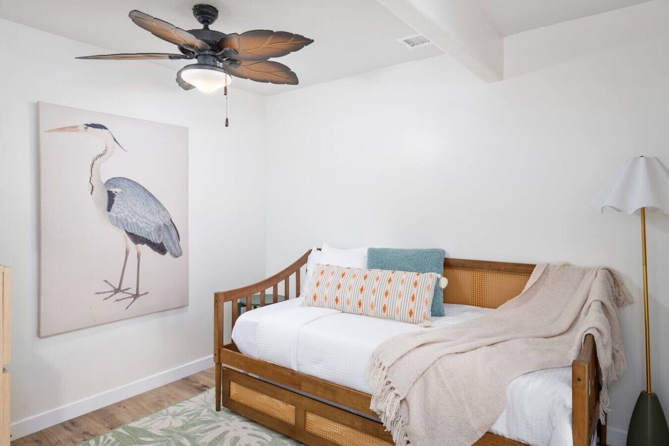Un dormitorio con una cama de madera, un ventilador de techo, una lámpara de pared y un cuadro grande de un pájaro.