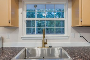 Eine Küche mit Spüle aus Edelstahl, einem Fenster mit Blick auf Bäume und Holzschränken.
