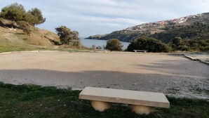A gravel area with a bench, a body of water, and hills in the background. - Holiday Home in 'Port Aloès' Resort with Sea View, Shared Pool and Air Conditioning (Cerbère)