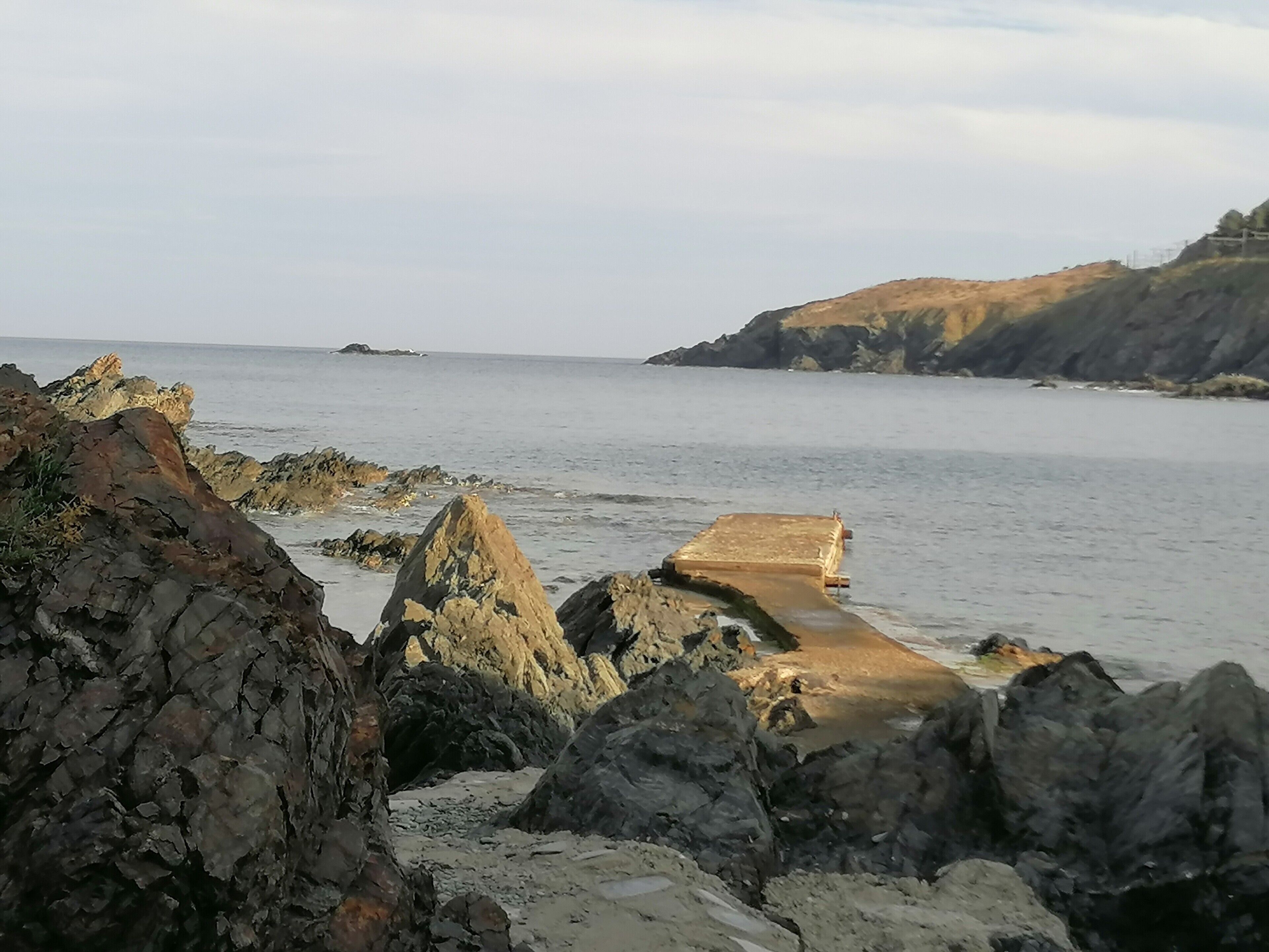 Une côte rocheuse avec une grande formation rocheuse au premier plan et une falaise en arrière-plan.