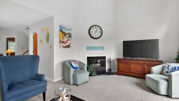 A living room with a blue armchair, a grey armchair, a flat-screen TV, a fireplace, and a clock on the wall.