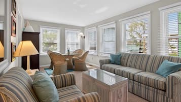 A living room with striped sofas, a glass coffee table, wicker chairs, and a lamp.