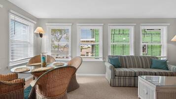 A room with a dining table, chairs, a sofa, and a window with blinds.