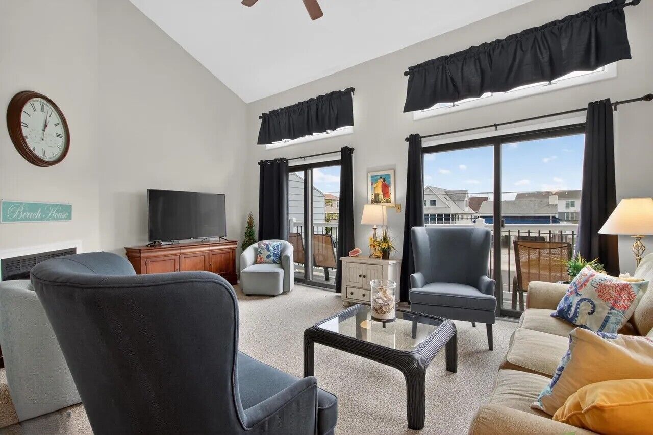 A living room with a flat-screen TV, two armchairs, a sofa, a coffee table, and a large window with curtains.