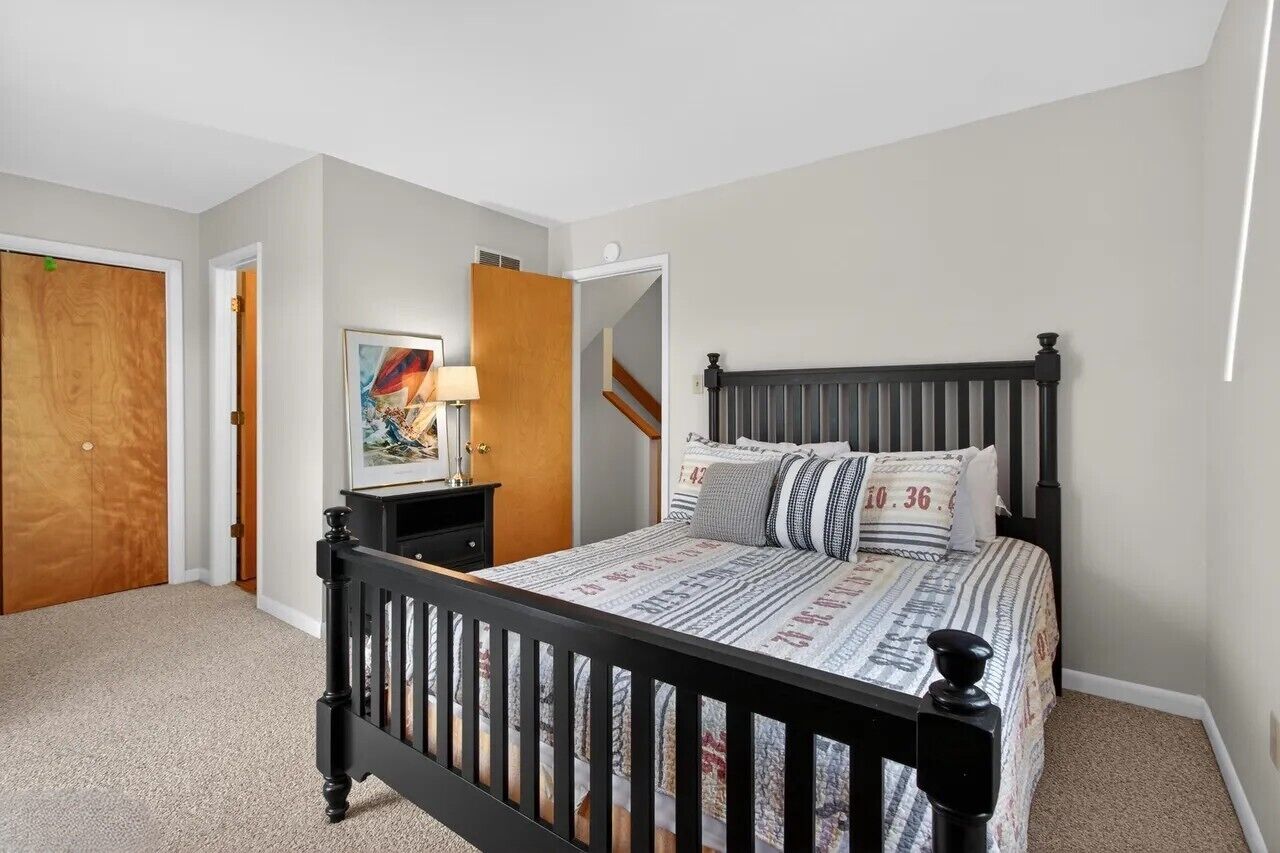 A bedroom with a bed, a nightstand, a lamp, and a door.