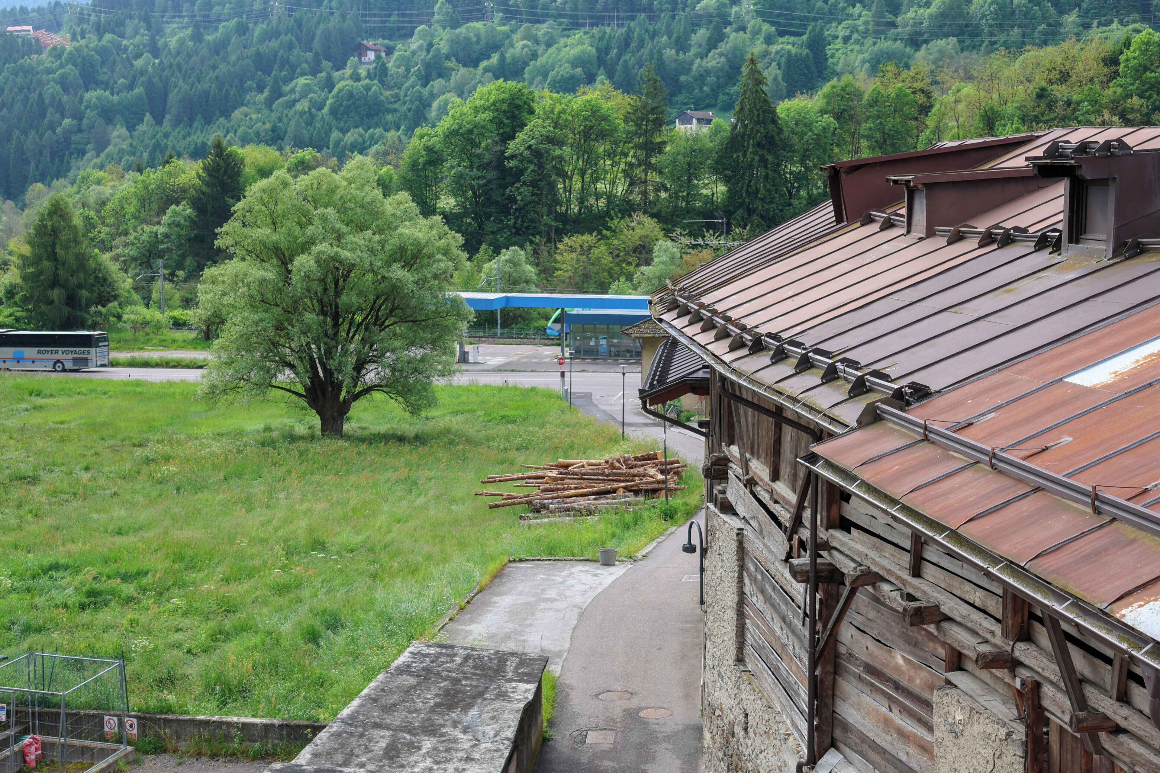 A building with a sloped roof, a paved pathway, and a green field with trees.