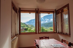 Ein Essbereich mit Tisch für zwei Personen, Blick auf eine Berglandschaft durch offene Fenster und ein Heizkörper an der Wand.