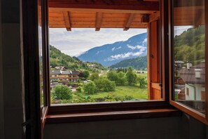 Ein Zimmer mit Holzboden und einem Fenster mit Blick auf eine grüne Landschaft mit Häusern und Bergen.