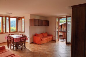 Ein Zimmer mit Esstisch, Stühlen, einer Couch und Blick ins Freie.