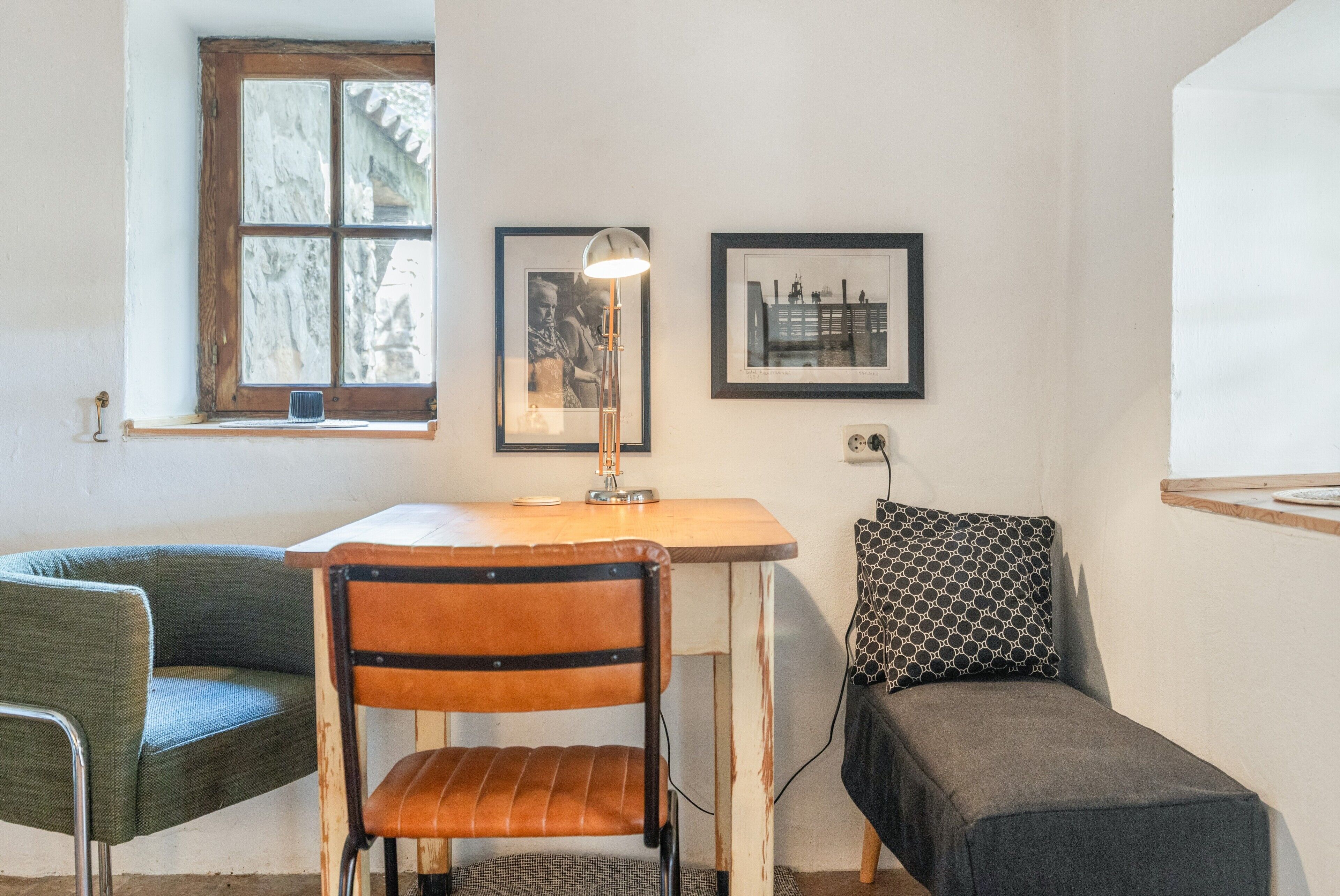 Een kamer met een houten tafel, een stoel, een bank, een lamp en twee afbeeldingen in lijsten aan de muur.