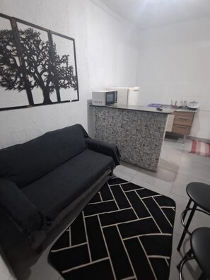 A compact living space with a sofa, a patterned rug, a kitchenette with a microwave, and a tiled floor. - Vrbo Property (São Paulo)