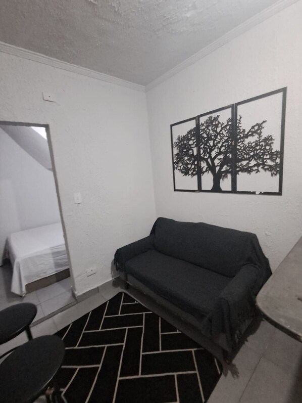 A small, sparsely furnished room with a sofa, a bed, a chair, and a black and white patterned rug. - Vrbo Property (São Paulo)