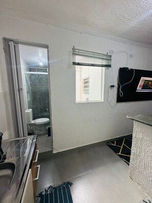 A small, compact bathroom with a toilet, a shower area, and a window with blinds. - Vrbo Property (São Paulo)