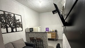 A compact living space with a sofa, a small dining area, a kitchenette, and a wall-mounted TV.