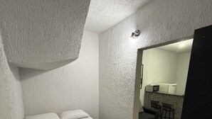 A bedroom with a bed, a small kitchenette, and a bathroom visible through an open door.