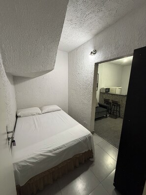 A bedroom with a bed, a small kitchenette, and a bathroom visible through an open door.
