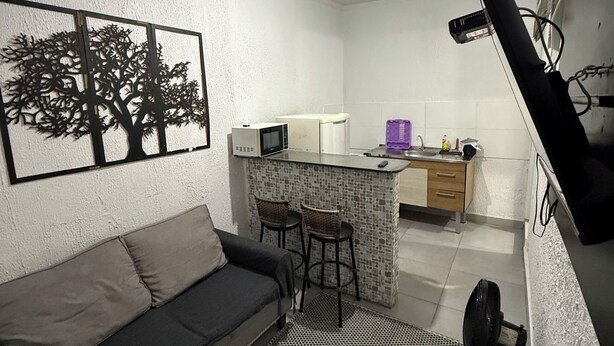 A compact living space with a sofa, a small kitchen area, a bar stool, and a ceiling fan.