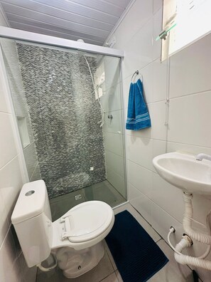 Een badkamer met een glazen douchecabine, een toilet, een wastafel en een blauwe handdoek aan de muur.