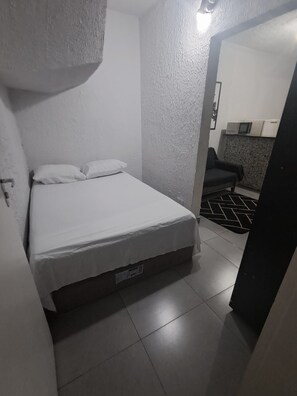 A small, compact room with a bed, a chair, and a kitchenette area. - Vrbo Property (São Paulo)