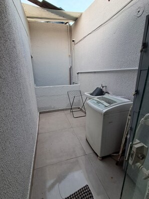 Een kleine, afgesloten wasruimte met een wasmachine en een droogrek.
